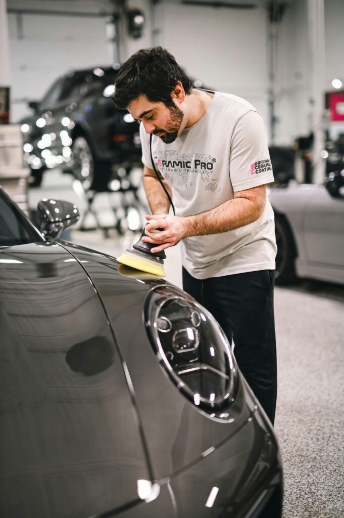 Man polishing a car hood in a professional garage setting, focused on detailing.