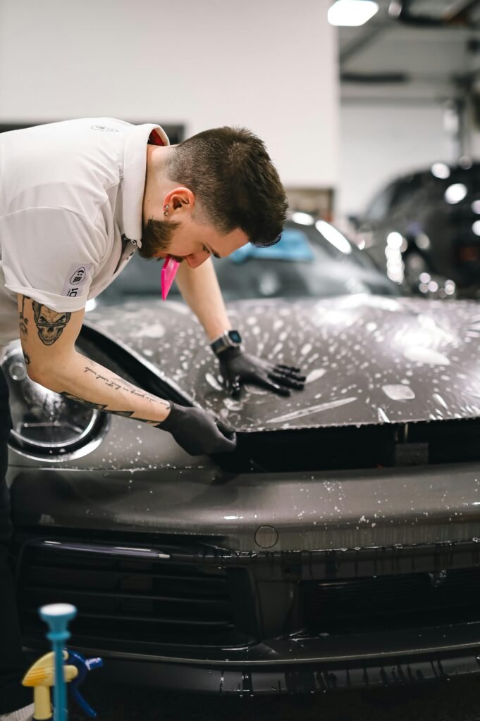 Man applying protective film to a sports car hood in an auto detailing workshop.