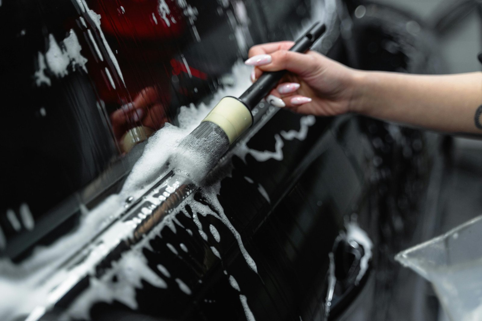 Detailed view of a car being washed, showing soap suds and a brush in action.